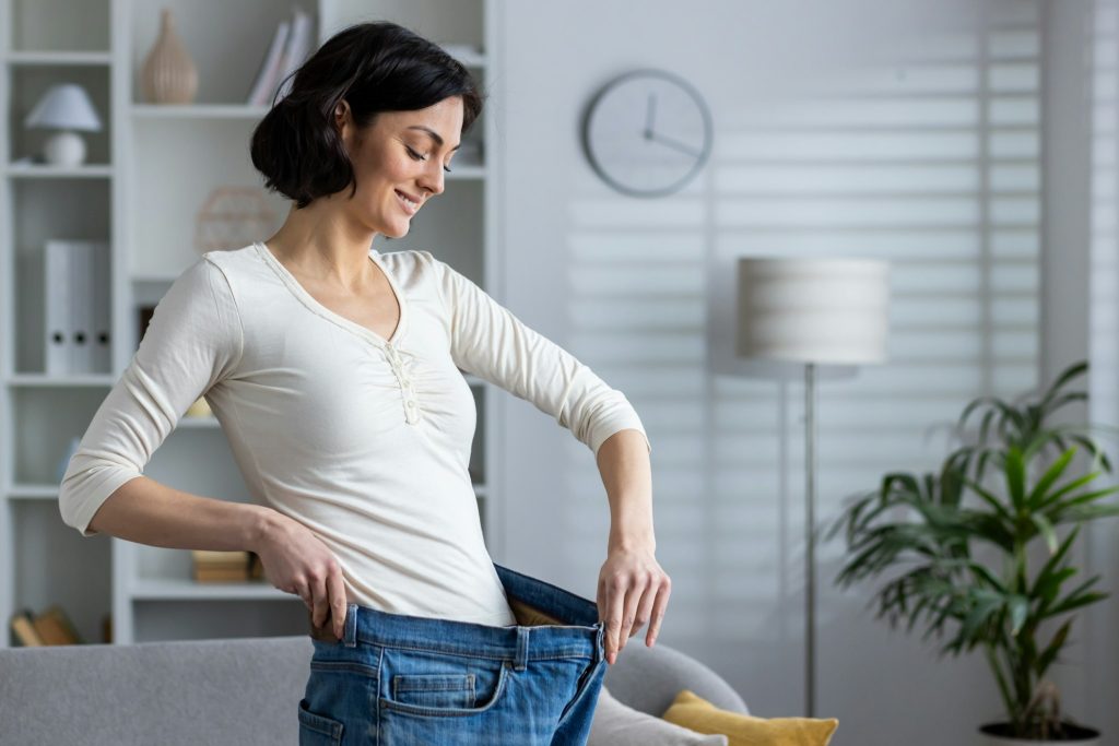 Happy woman showing weight loss by wearing old jeans at home